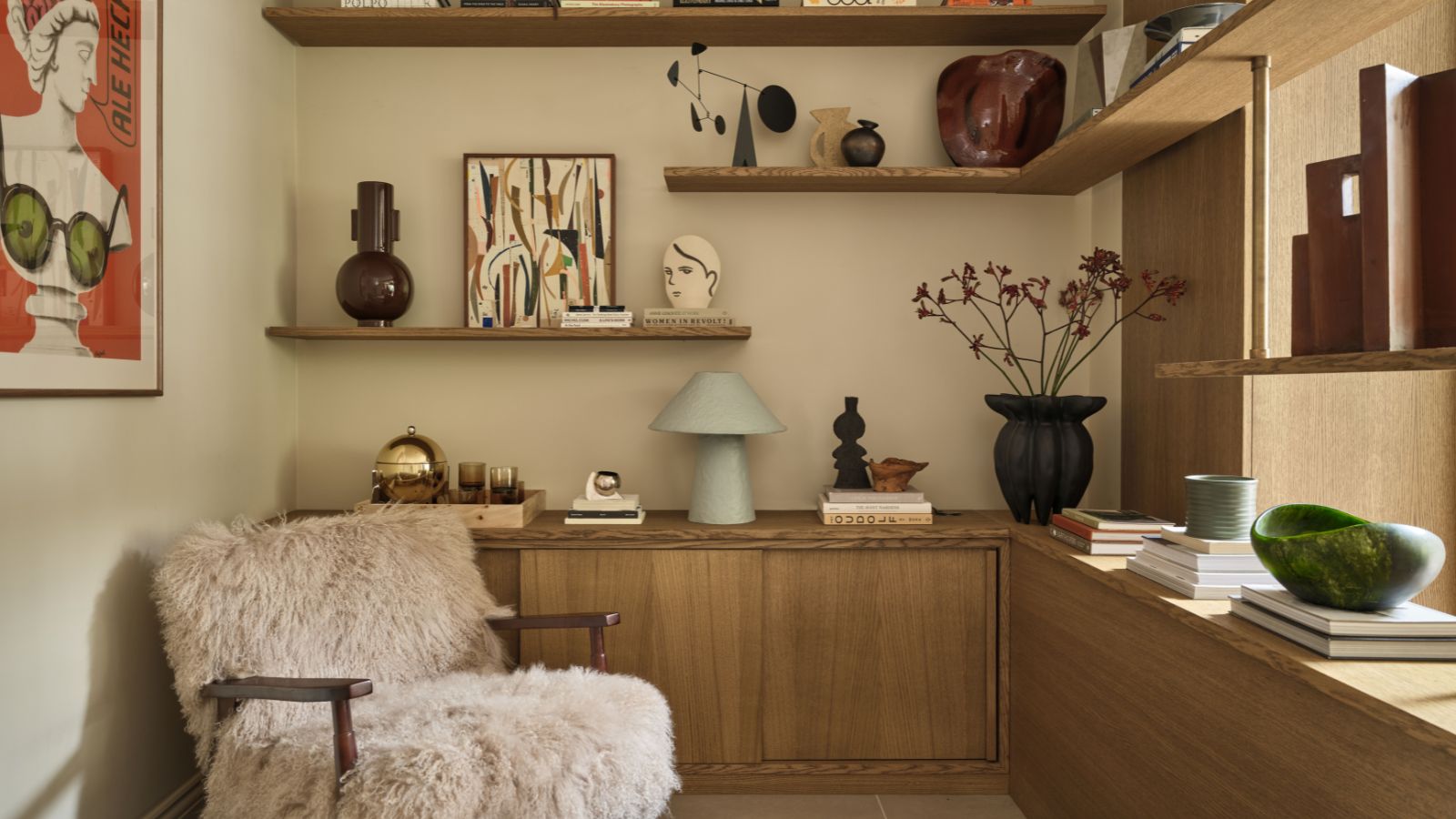 Reading corner with wooden shelves decorated with vases and artwork, a fluffy armchair, and a large red print on the wall