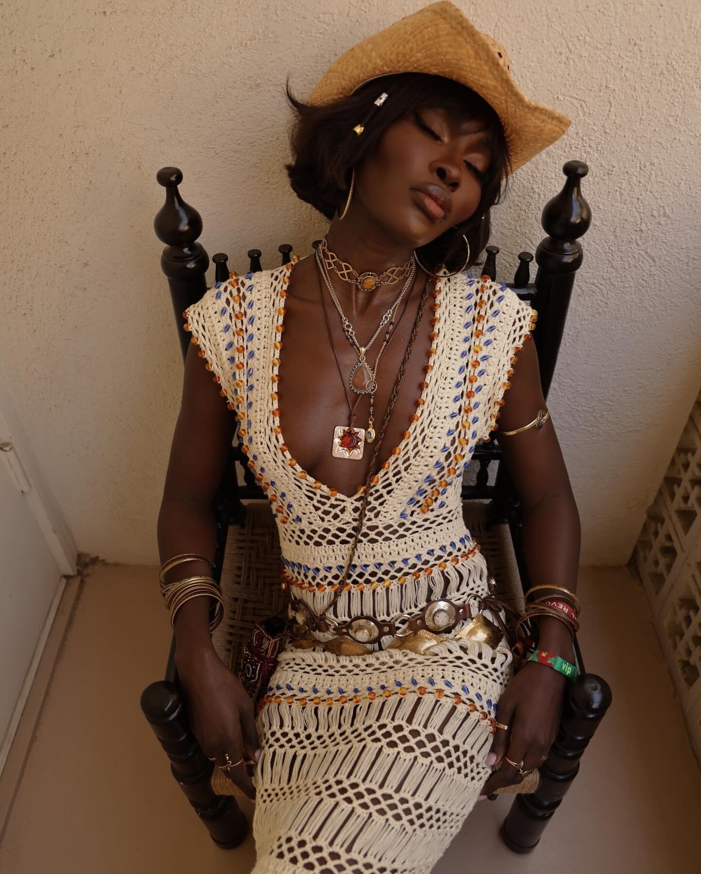 Fashion person Amy wears a crochet multi coloured dress, Western style belts a cowboy crochet hat and a stack of necklaces with western themes she is sat in a chair in a image taken from her Instagram recently.
