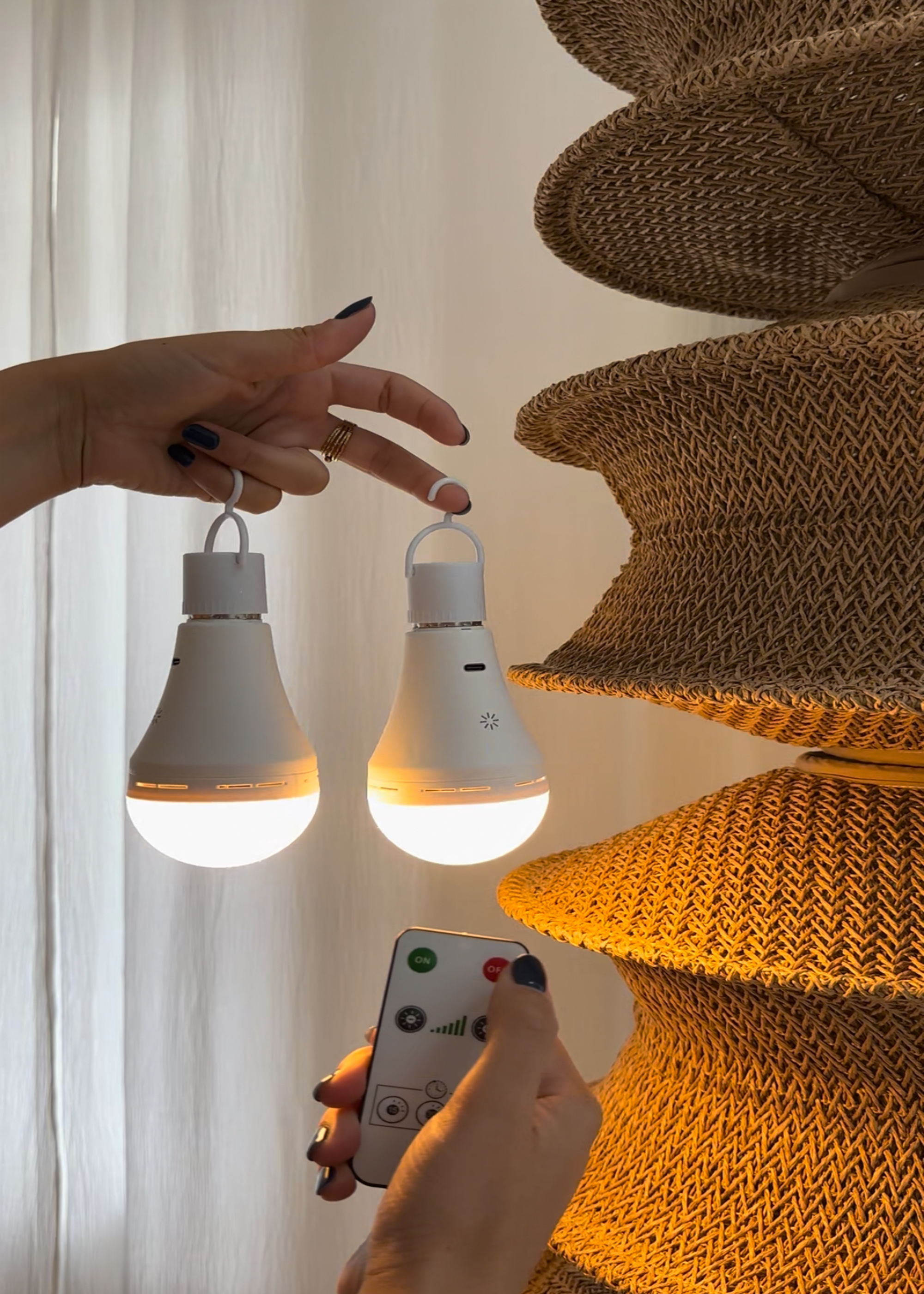 A close up of a woven lampshade with a hand holding up two wireless lightbulbs