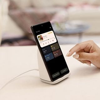 An image of a Pixel 6 resting on a Pixel Stand, with a user interacting with the ambient display interface, including the Performance and Quiet mode charging options.