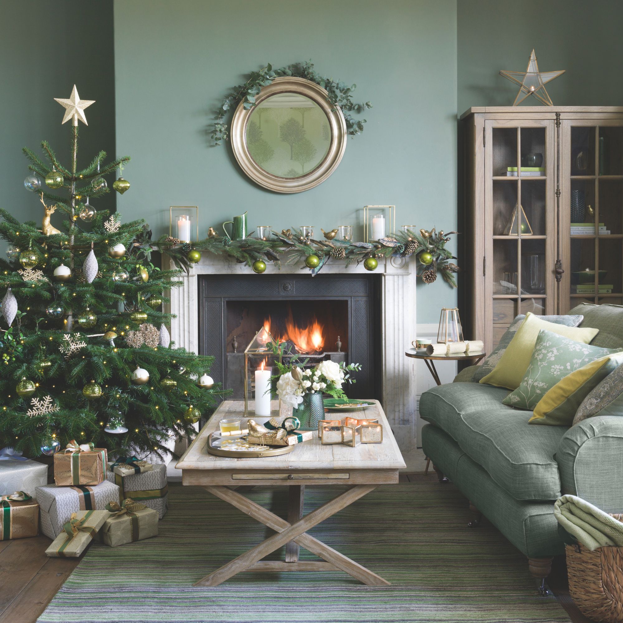 Festive living room with green painted walls, a green sofa and an open fireplace with a wooden coffee table in front of it