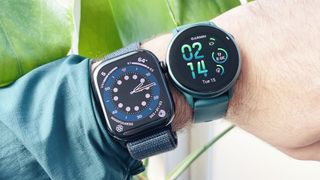 Close-up of a user's wrist wearing both the Apple Watch 10 on a blue fabric strap (left) next to the Garmin Vivoactive 6 (right) on an emerald green strap