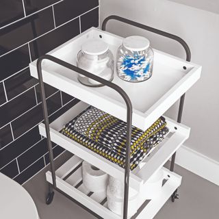 A black-tiled bathroom with a wheeled shelving unit