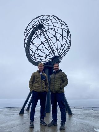 Phil MacHugh and Martin Compston stand in front of a wire globe structure at their final stop at Nordkapp in the Arctic Circle