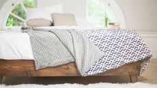  picture of a cooling weighted blanket draped over the end of a bed with a wooden bedframe
