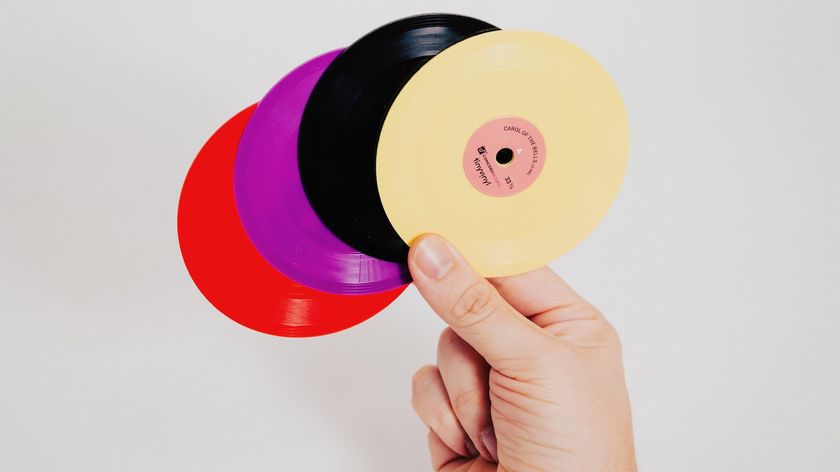 Four Tiny Vinyl 4-inch discs of varying colours fanned out while being held between a thumb and first two fingers of a right hand.