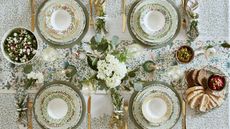 Tablescape with green William Morris print tablecloth, matching charger plats, gold flatware and white floral arrangements