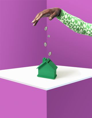 Homebuyers money-saving hacks: studio shot of hand dropping pound coins into green house money box in studio set.