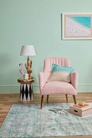 A pastel pink armchair and lamp-topped side table against a mint green background