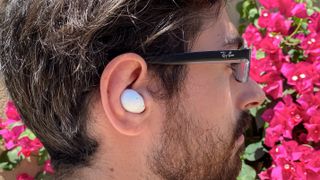 The Samsung Galaxy Buds Live earbuds in white pictured in someone's ear against a pink, flower background.