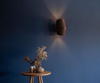 wireless wall light made from oak on blue painted wall above small wooden table with dried flowers in vase