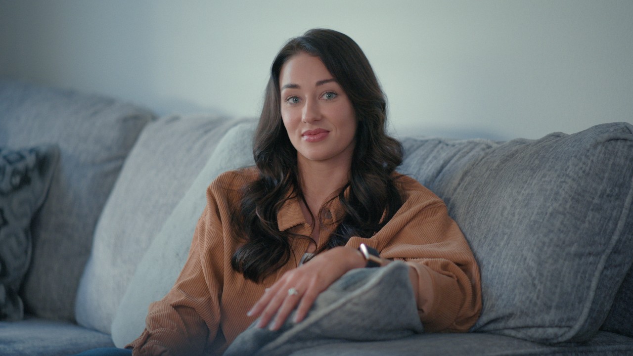 Kelcey Wetterberg sitting on her couch with her left hand laying on a pillow.