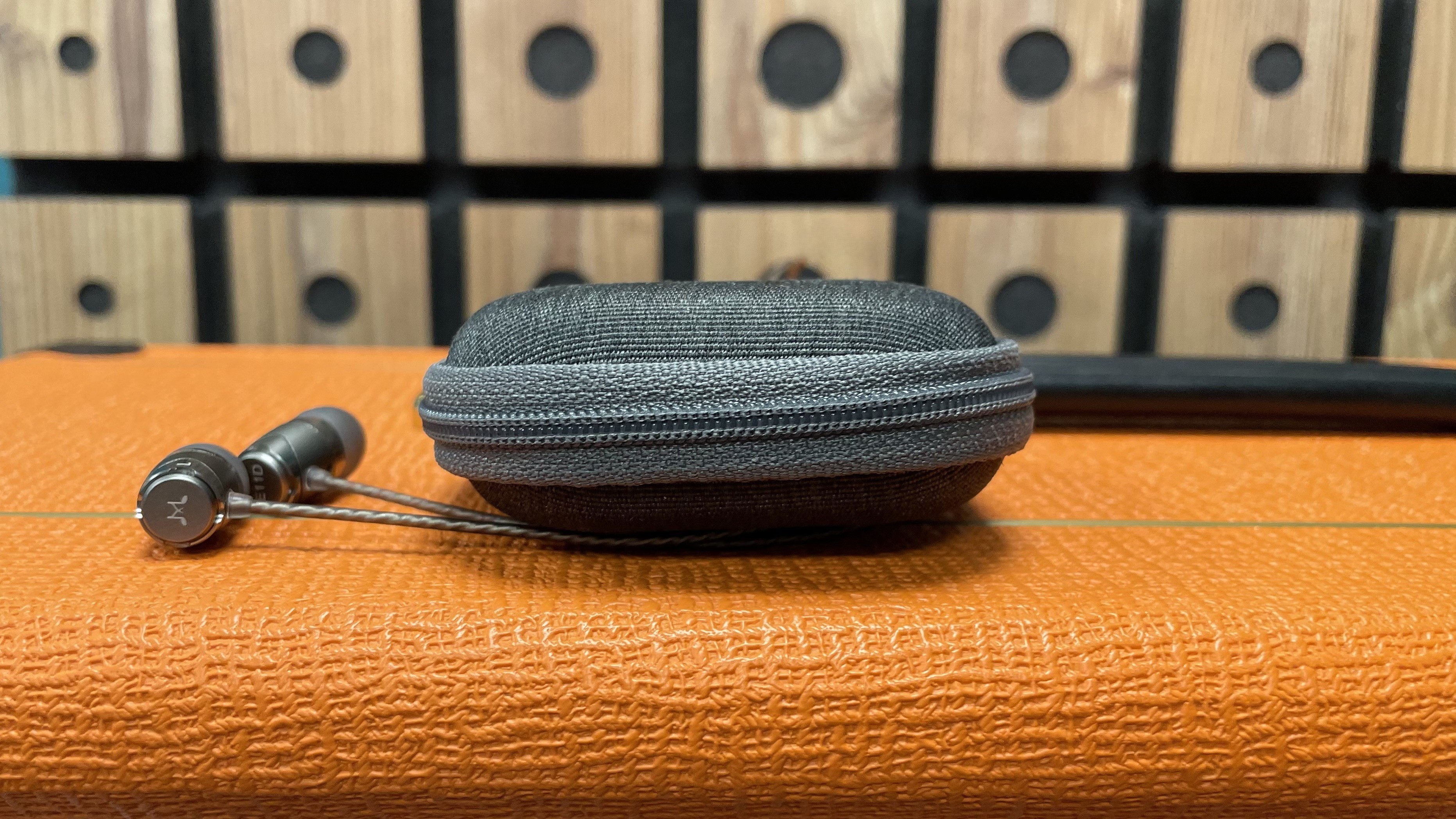 SoundMagic E11D earbuds and gray carry case on top of orange amp