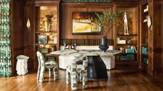 Dining room with built-in wooden shelving and alcoves with glossy metallic Fromental wallpaper, statement chairs and artful decor