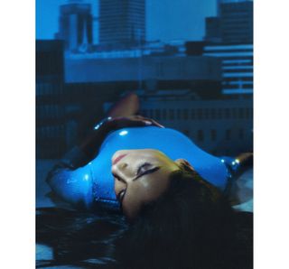 Simone Ashley laying down in front a cityscape backdrop wearing a blue sequin dress.