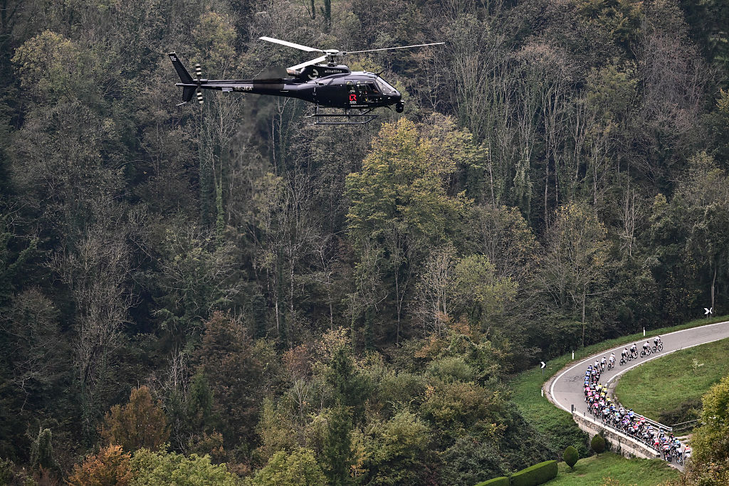 A live broadcast helicopter hovers overhead as the peloton cycles in the Passo Della Crocetta ascent during the 119th edition of Il Lombardia