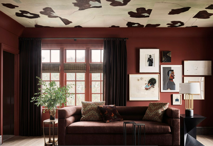 a red painted living room with a maroon sofa and large wall art