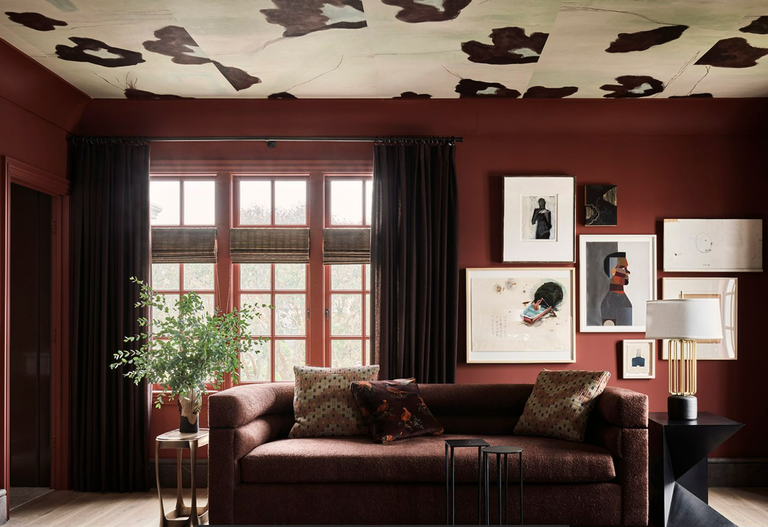 a red painted living room with a maroon sofa and large wall art
