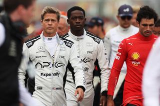 brad pitt as an f1 driver leading a team of racers in their white racing suits in a still from the movie f1