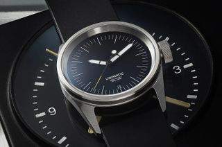 small black-dial steel watch with black strap seen above a clock face