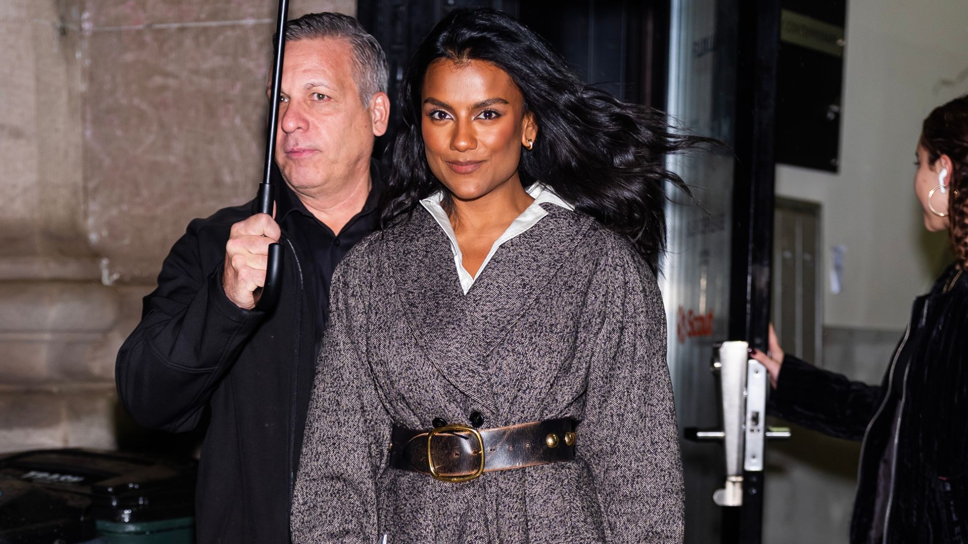 Simone Ashley walks outside in New York wearing black carpi leggings with a tweed belted jacket and mole suede heels.