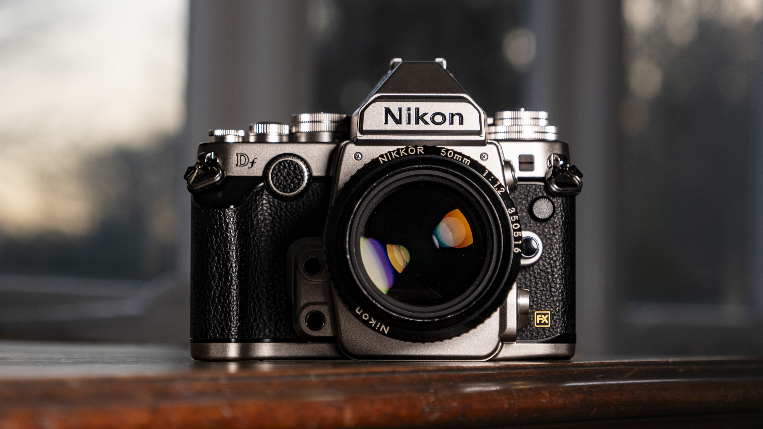 Nikon Df DSLR camera on a wooden surface by large window, with dusk light