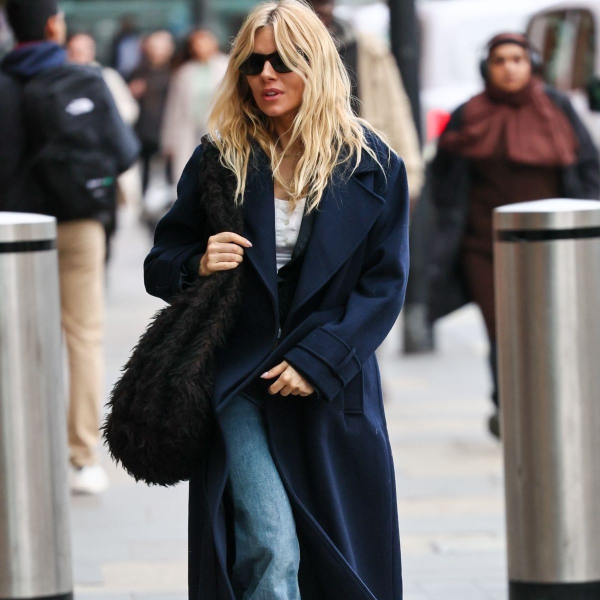 Sienna Miller wearing navy coat, blue jeans and white tank top.