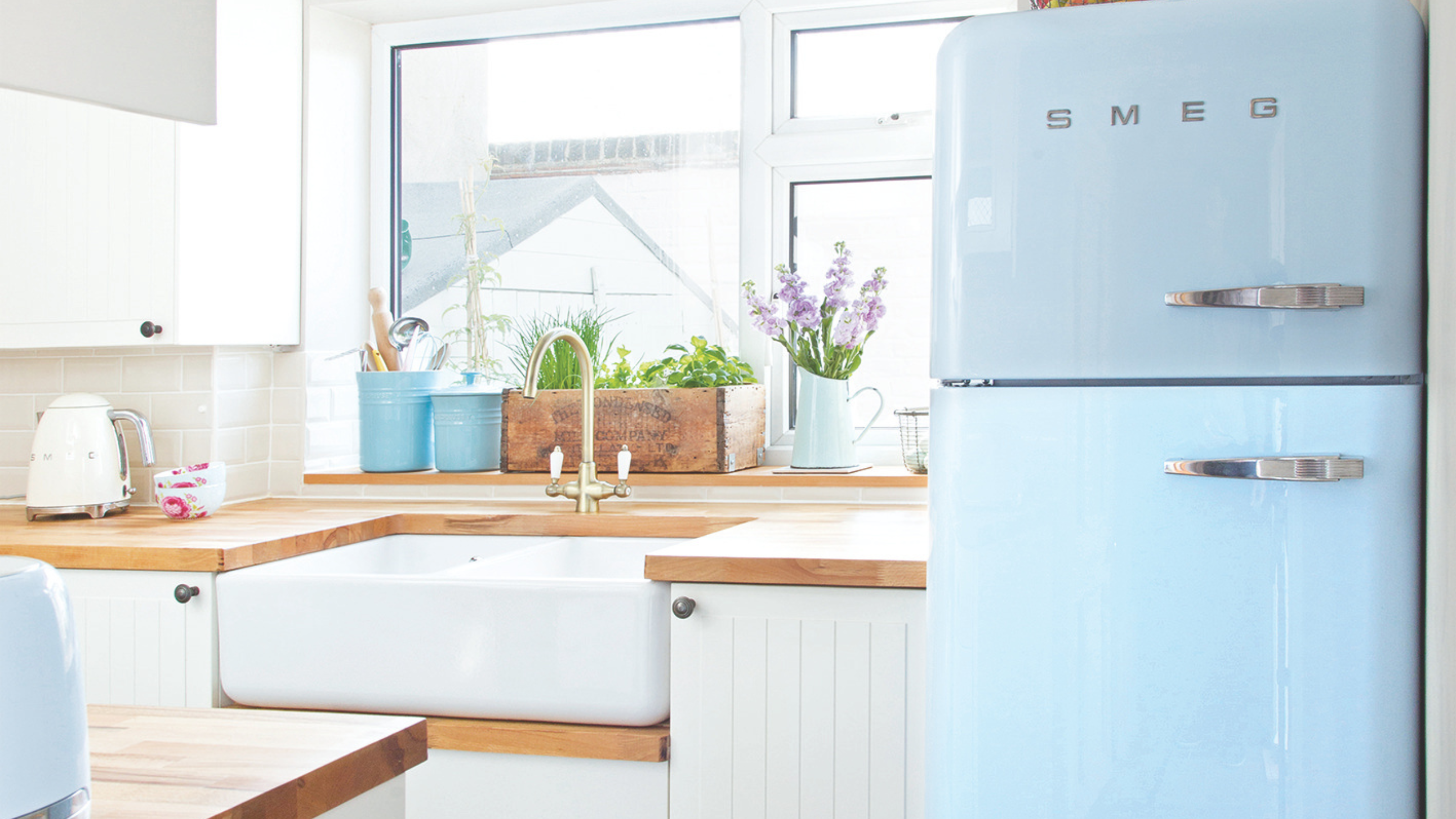 Pale blue smeg fridge in a rustic kitchen. On the wooden side board is a white smeg fridge.