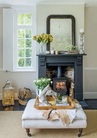 Dark mantelpiece and hearth with mirror and a woodburner set in a pale grey wall beside a window