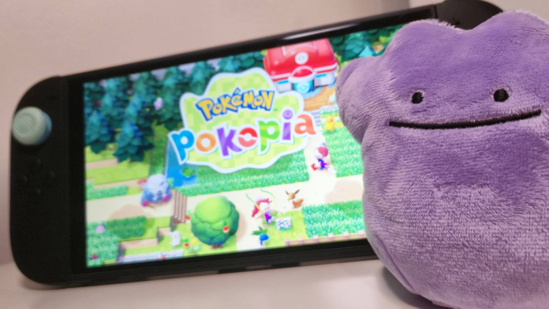 Photo of a Ditto plushie sitting in front of a Nintendo Switch 2 handheld.