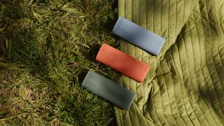 Sonos Roam 2 in three colours (red, green and blue) on a green camping mat and grass.