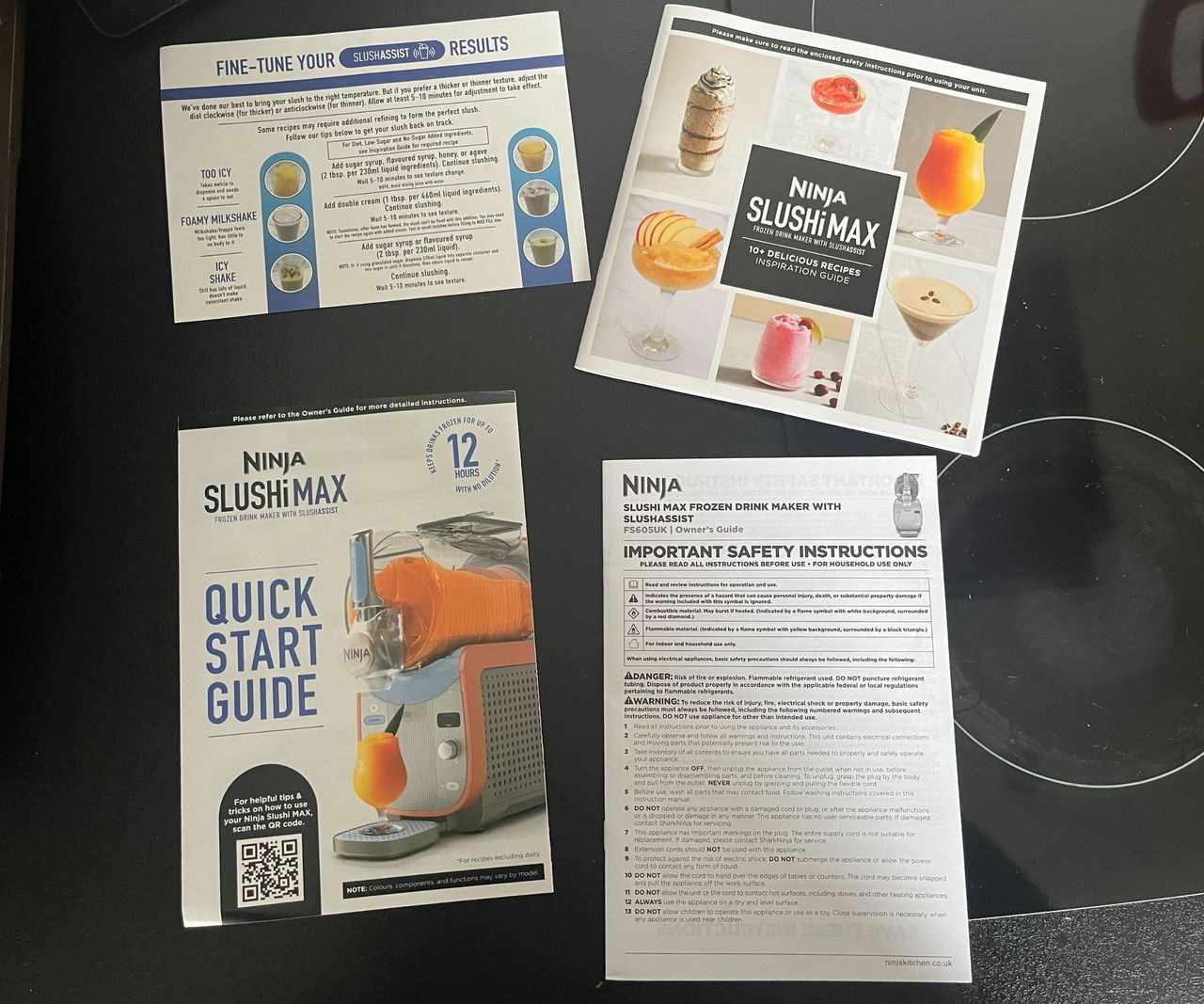 A set of four instruction manuals for the Ninja Slushi Max on a black glass stove top.