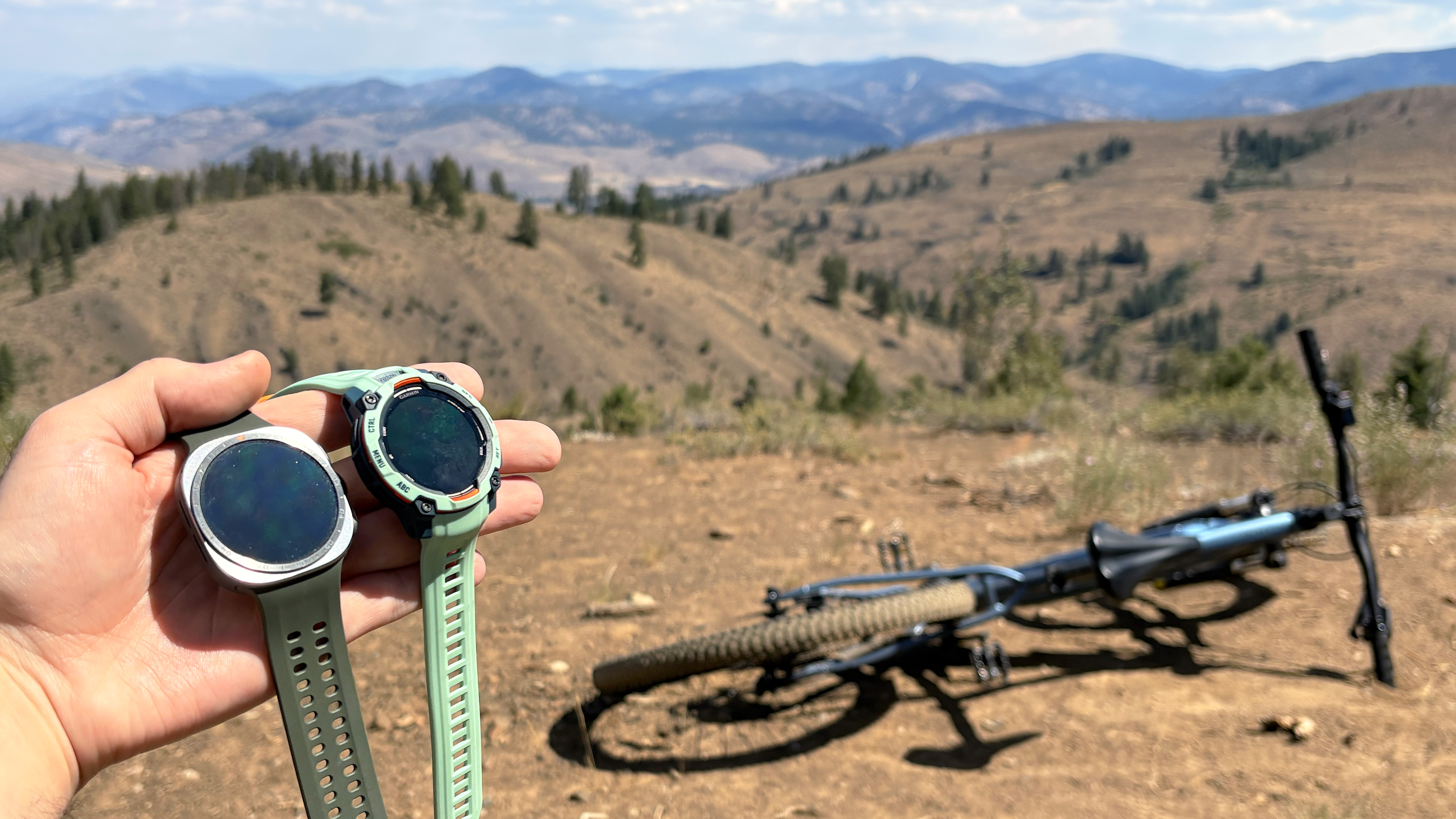 Close-up of the Samsung Galaxy Watch Ultra 2 and Garmin Instinct 3 in the mountains during an e-biking excursion