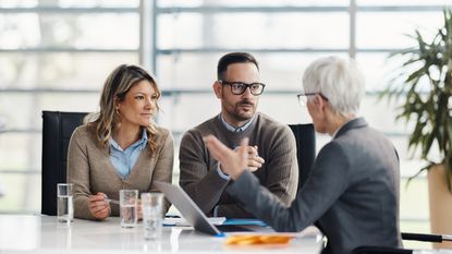 A couple listen intently at a conference table in an office as their financial adviser talks.