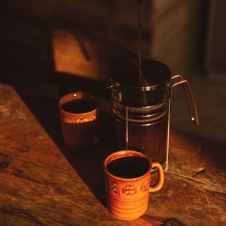 A French press with two mugs of coffee on a wooden dining table