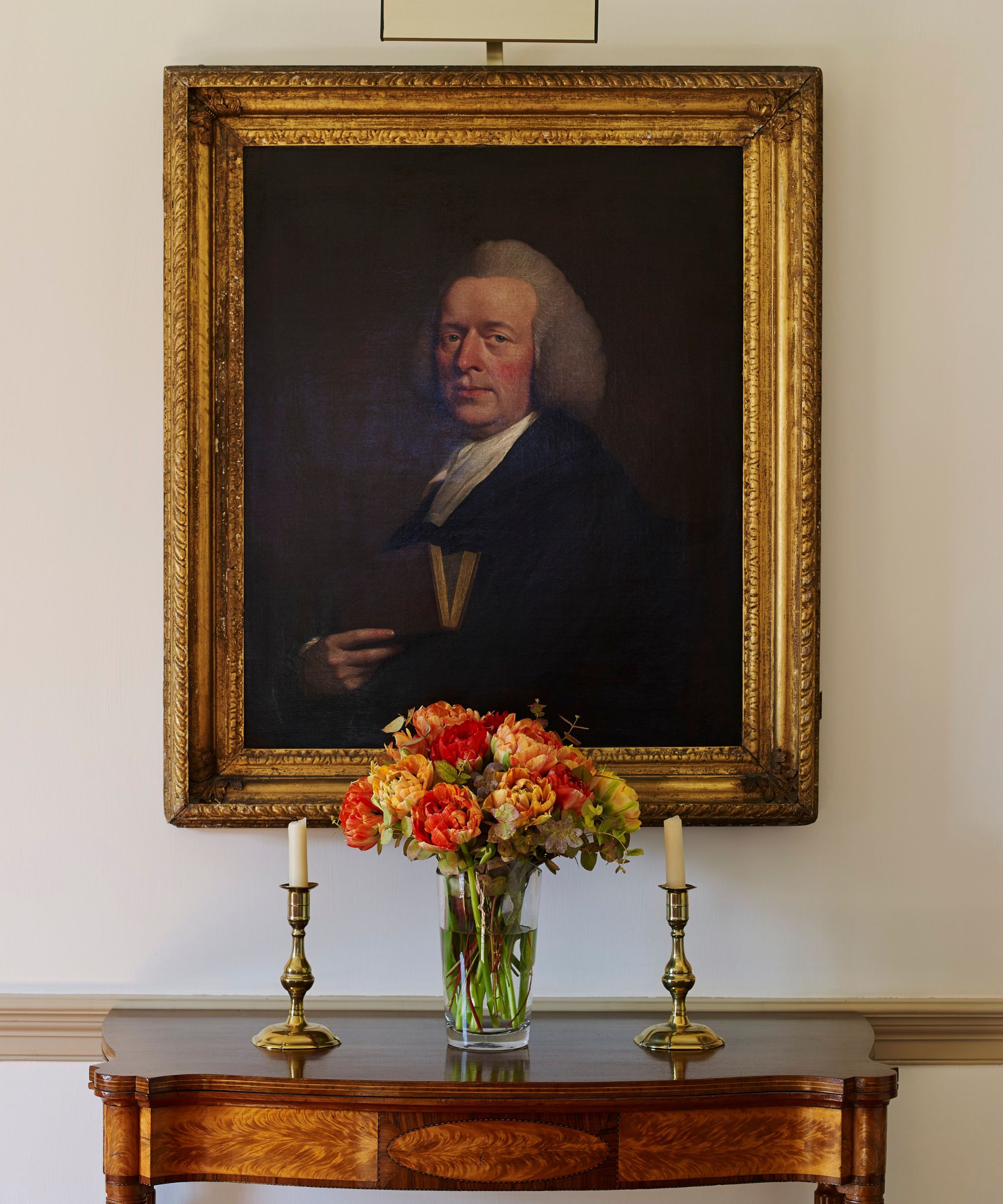 Hallway with antique wood table, two gold candlesticks, bouquet and antique painting with ornate gold frame