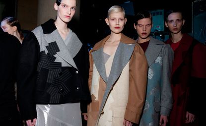 One model with a black and grey coat, one with a brown, cream, and grey coat, with people in the background