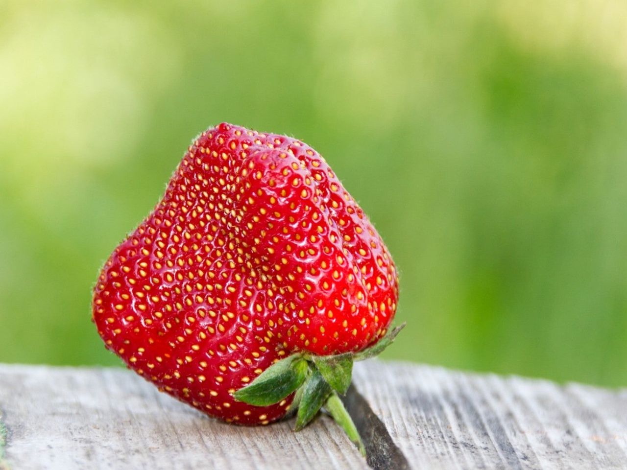 A weirdly shaped strawberry sits on a wooden surface