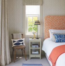 bedroom with pale taupe walls and bed with upholstered headboard in orange print fabric and side table with stripe table lamp