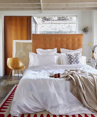 bedroom with beamed ceiling, stone floor, leather headboard, designer modern chair, white silk bedding, white walls