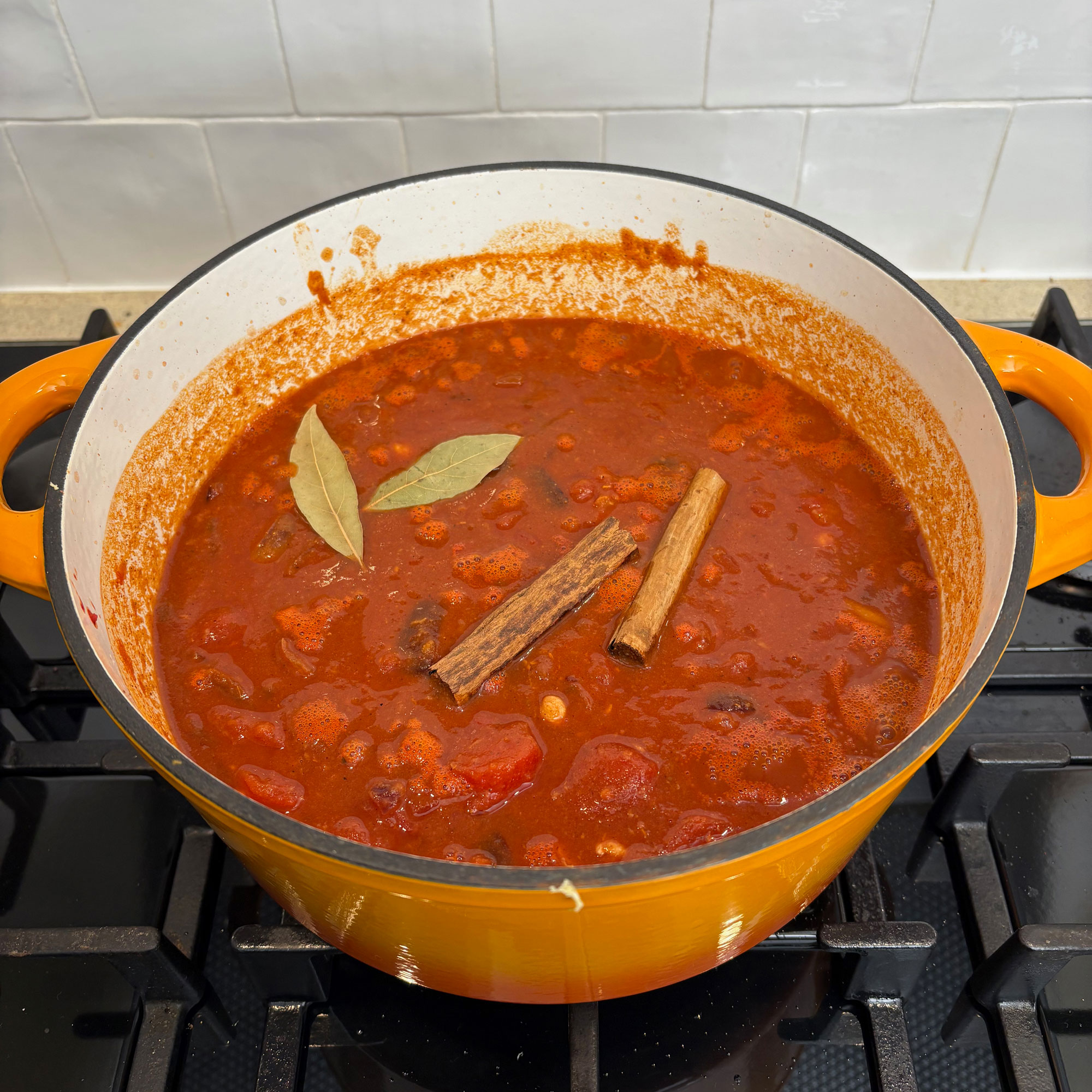 Orange cast iron pan on black hob with red stew with cinnamon sticks and bay leaves