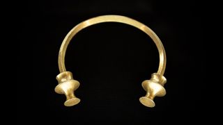 A golden C-shaped bracelet against a black background. 