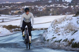 Male cyclist riding up a snowy lane wearing a pale blue Castelli Espresso Thermal Jersey