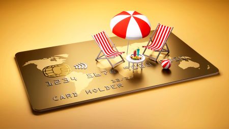 Beach chairs with table and cocktails and umbrella on a large golden credit card 