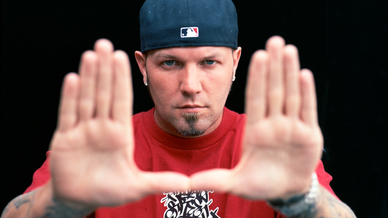 Fred Durst in a black cap holding his hands up to the camera 