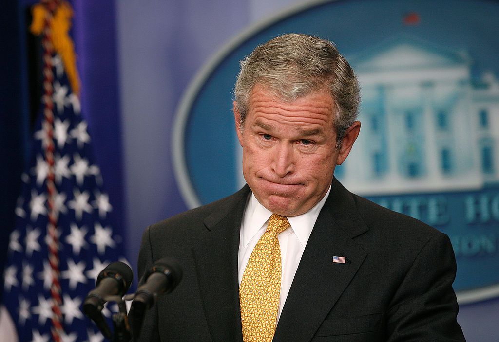 George W. Bush looks frustrated, pursing his lips and puffing his cheeks.