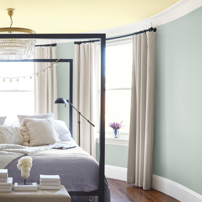 calm green bedroom with yellow ceiling and black four poster bed