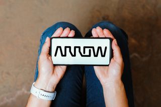 Arrow Electronics logo on a smartphone held in the palms of two two open-faced hands resting on a sitting person's lap