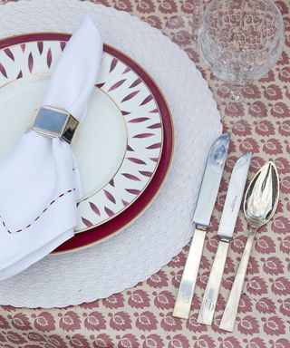 A close-up shot of a table place with red and white plates underneath a napkin next to cutlery