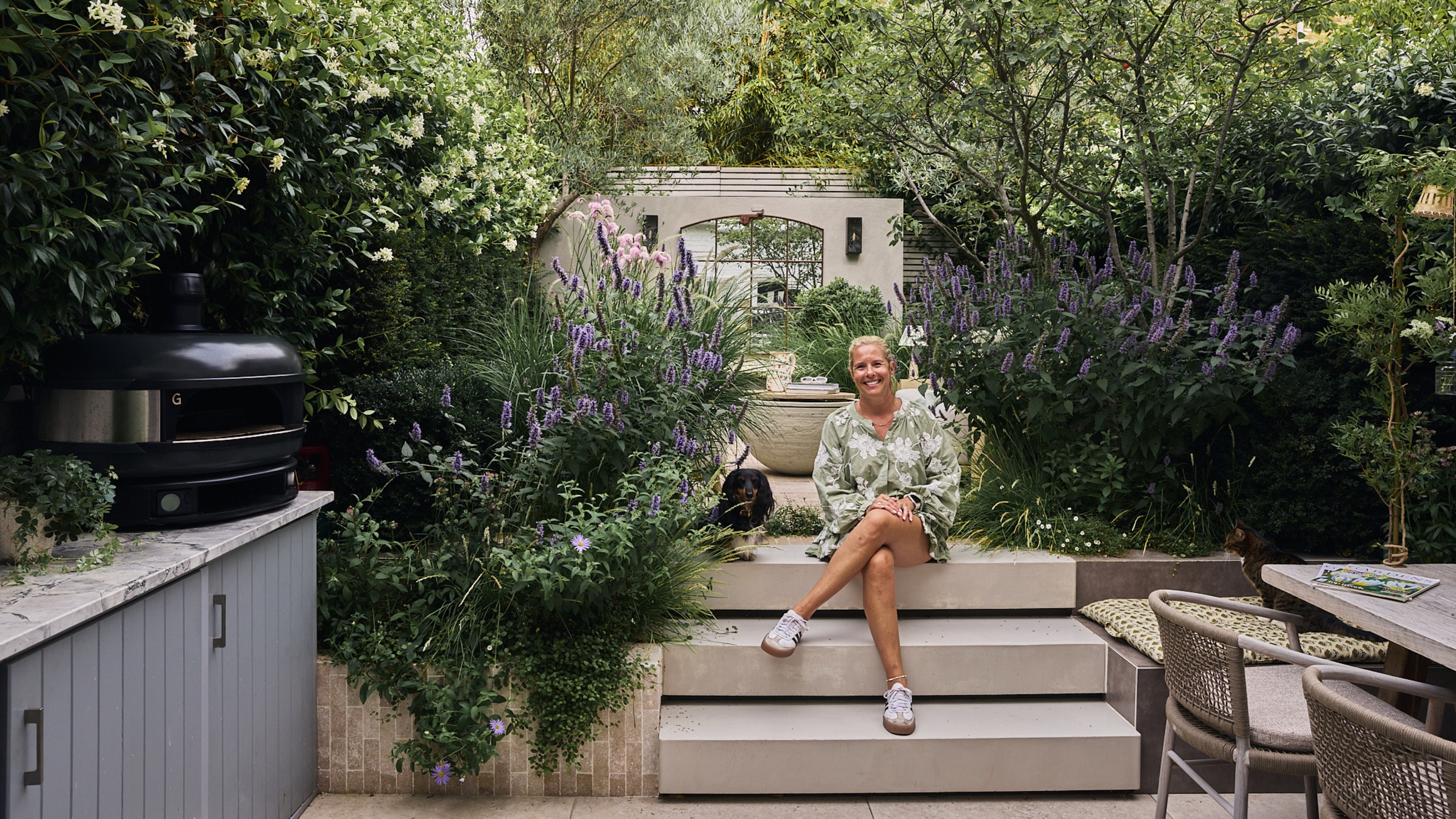 a woman and a dachshund in a modern garden surrounded by purple planting 